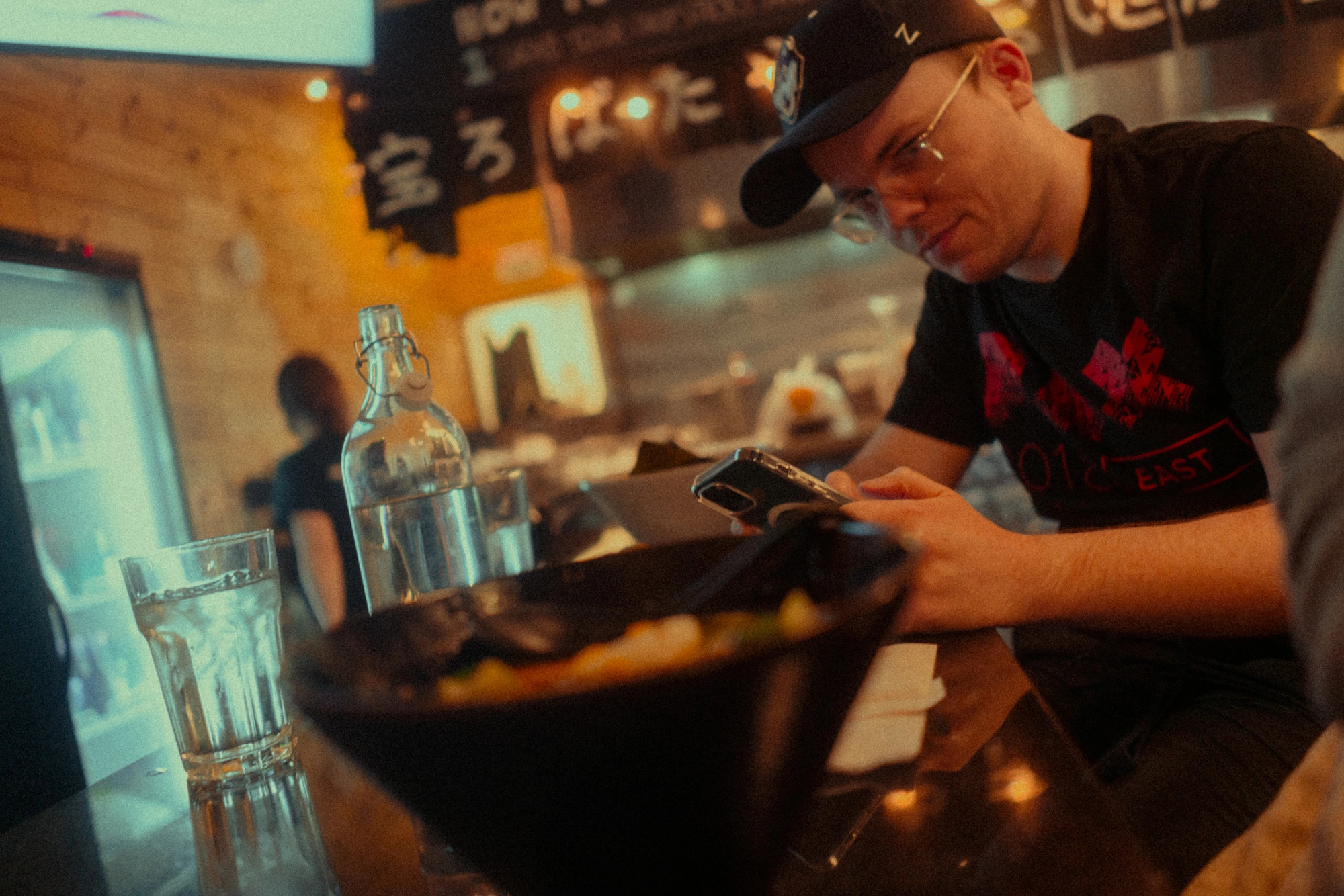Mike Tarpey eyeing the bowl of ramen that was just delivered to the table. Lighting is warm and blurred Japanese signage is visible in the background. Photographed by Trevor Wentt of trevorwentt.com.